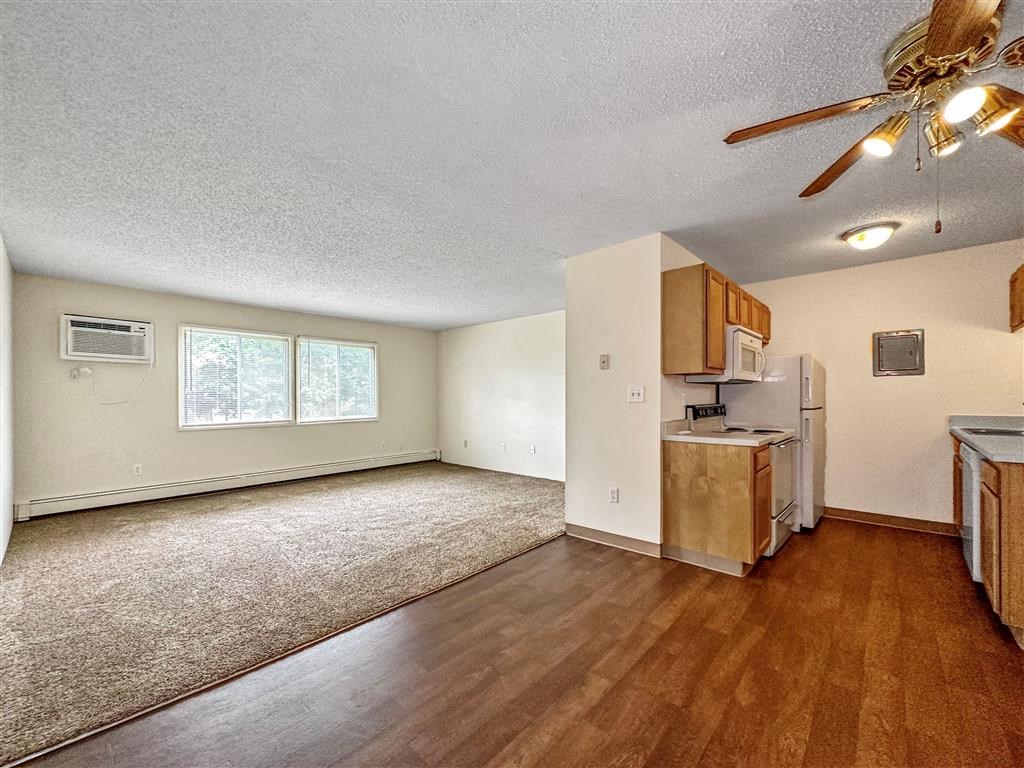 an empty living room with a kitchen and a ceiling fan at Foxwood Apartments, Indianola, 50125  