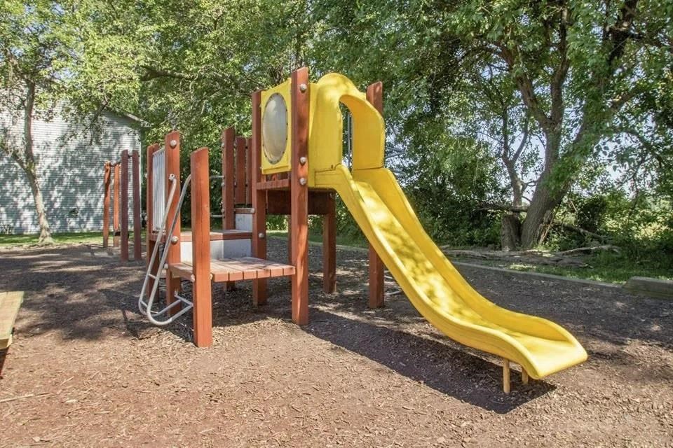 a playground with a slide and chairs in a park a playground with a slide and chairs in a park at Hunters Run Apartments, Newton, IA