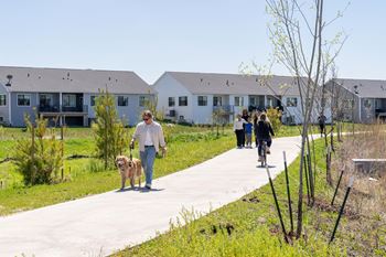 a man walking his dog down a sidewalk in front of houses at Rialto Townhomes Apartments, Iowa