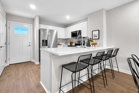 A kitchen with white cabinets and a white island with four black chairs.