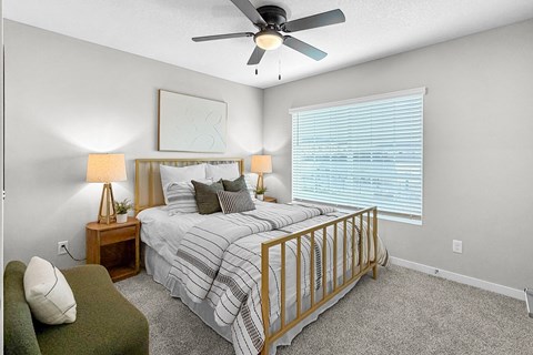 A bedroom with a bed, a green chair, and a ceiling fan.