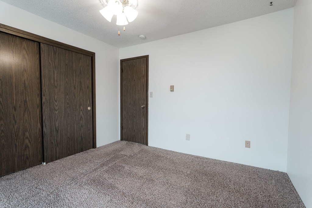 A room with a carpeted floor and two wooden doors. at Bristol Ridge, Urbandale, Iowa