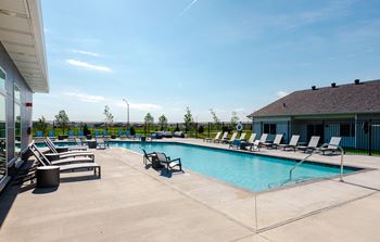 A pool area with sun loungers and a building in the background.at Converge NW, Waukee  