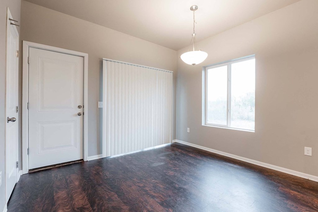 A room with a white door, a window with blinds, and a wooden floor. at Danamere Village, Carlisle, Iowa