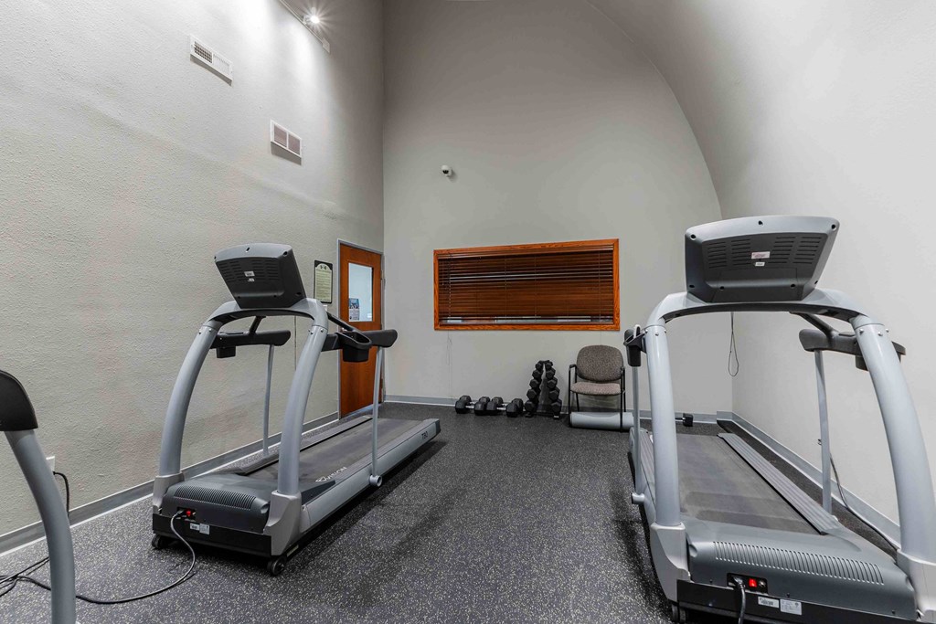 Two treadmills in a room with a grey carpet.