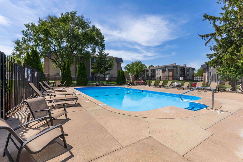 A pool surrounded by chairs and trees.