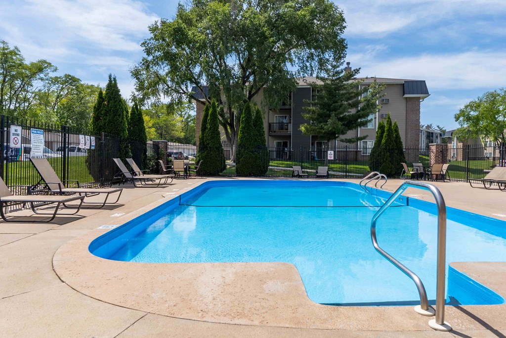 A blue swimming pool surrounded by trees and chairs.