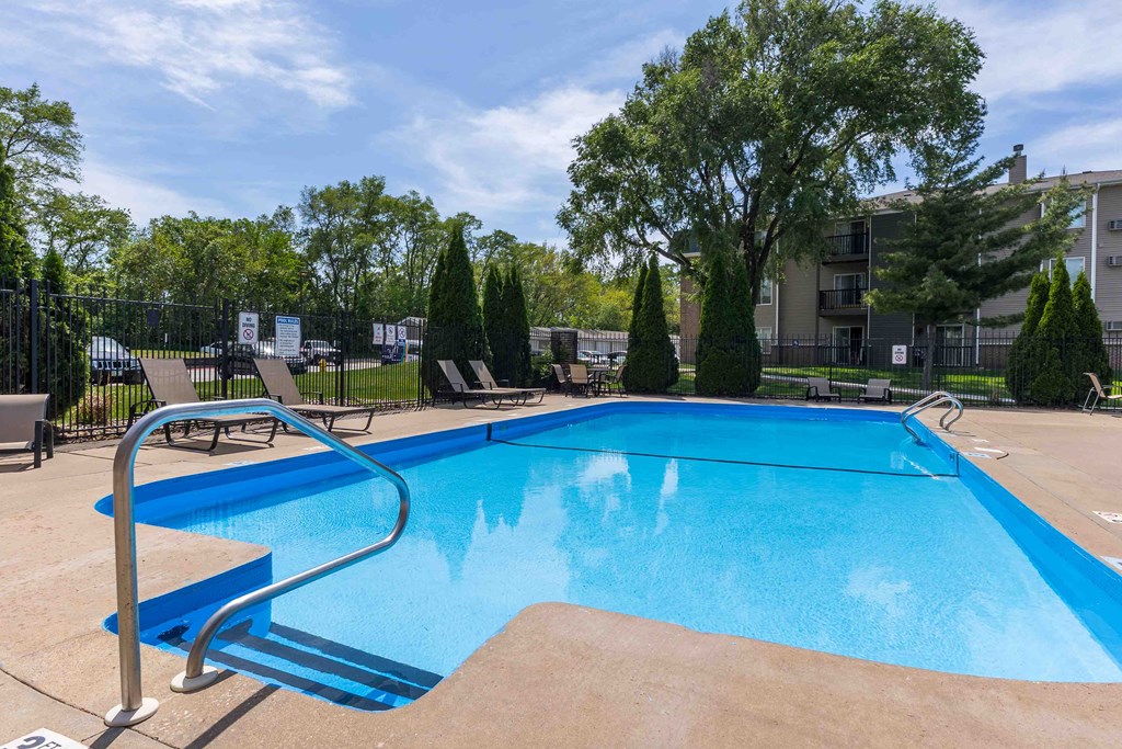A blue swimming pool surrounded by trees and a fence.