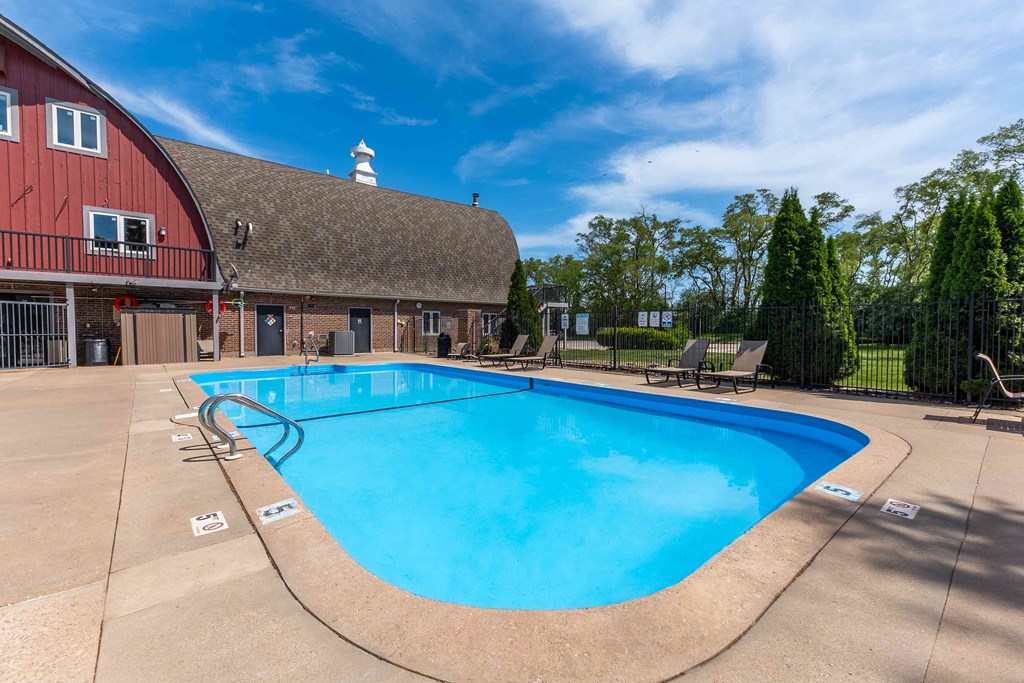 A large outdoor swimming pool with a red barn in the background.
