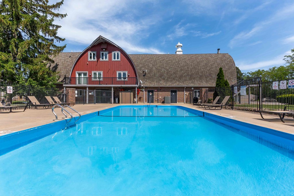 A large blue swimming pool in front of a red barn.