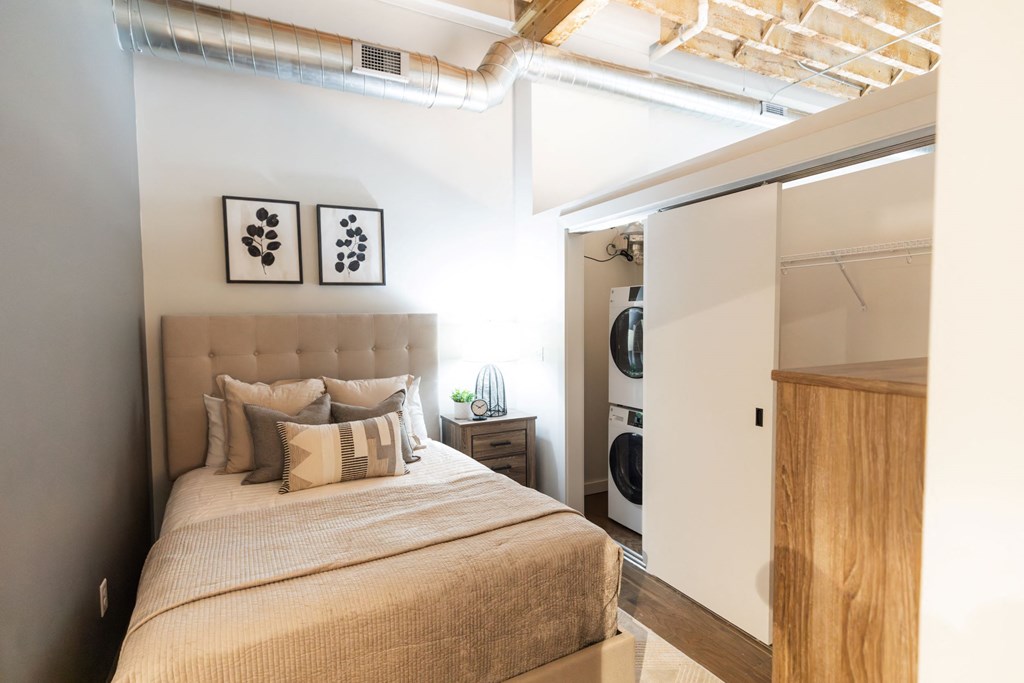 A bedroom with a bed, pillows, and a washing machine in the laundry area. A bedroom with a bed, pillows, and a washing machine in the laundry area.at Plant 1 Lofts, N. Newton, 50208
