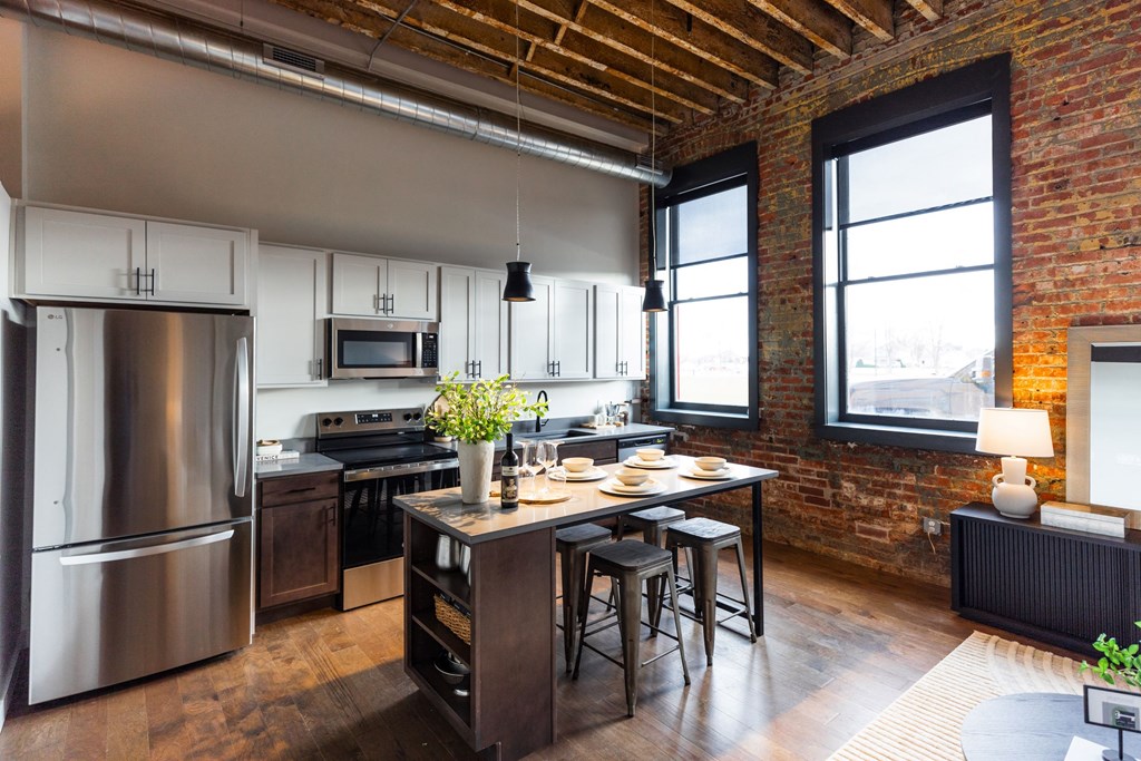 A kitchen with a large stainless steel refrigerator and a wooden table with chairs. A kitchen with a large stainless steel refrigerator and a wooden table with chairs.at Plant 1 Lofts, N. Newton, IA 50208