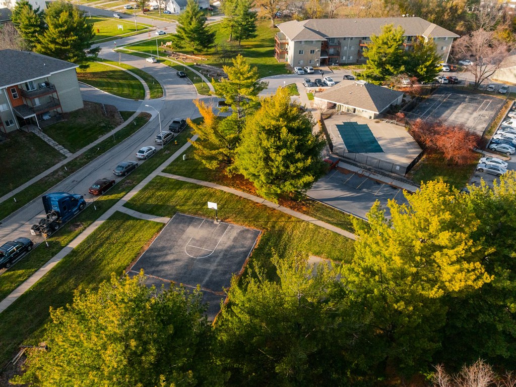 A basketball court is surrounded by trees and a parking lot. at Rosemont Place Apartments, Iowa