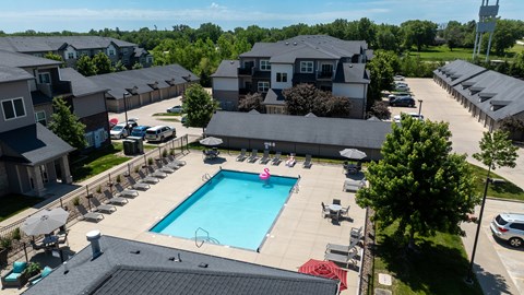 A large swimming pool surrounded by lounge chairs and umbrellas in a residential area.