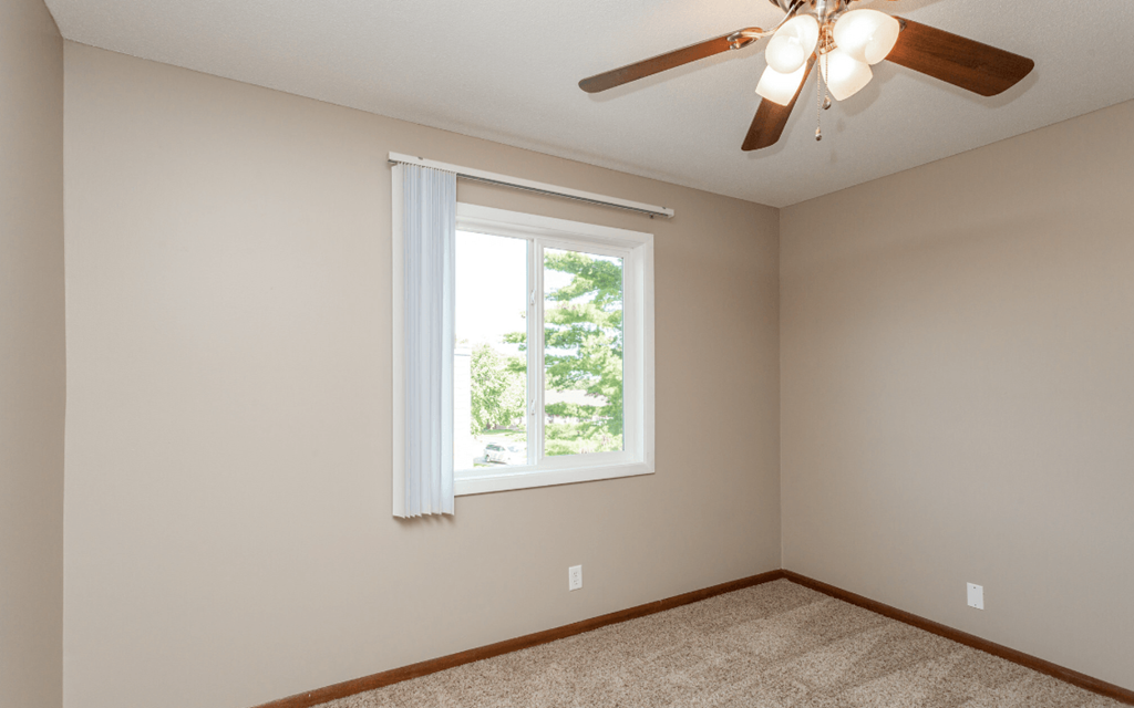 an empty bedroom with a ceiling fan and a window at Lake Shore Place Apartments, Ankeny, IA