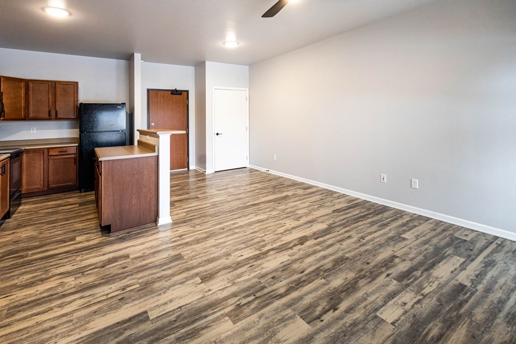 A room with wooden flooring and a kitchen area with cabinets and a counter at Meadowlark Place Apartments, Georgia