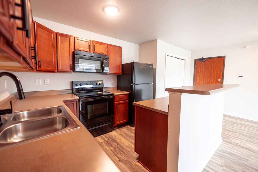A kitchen with wooden cabinets and a black refrigerator at Meadowlark Place Apartments, Grimes, IA,  50111
