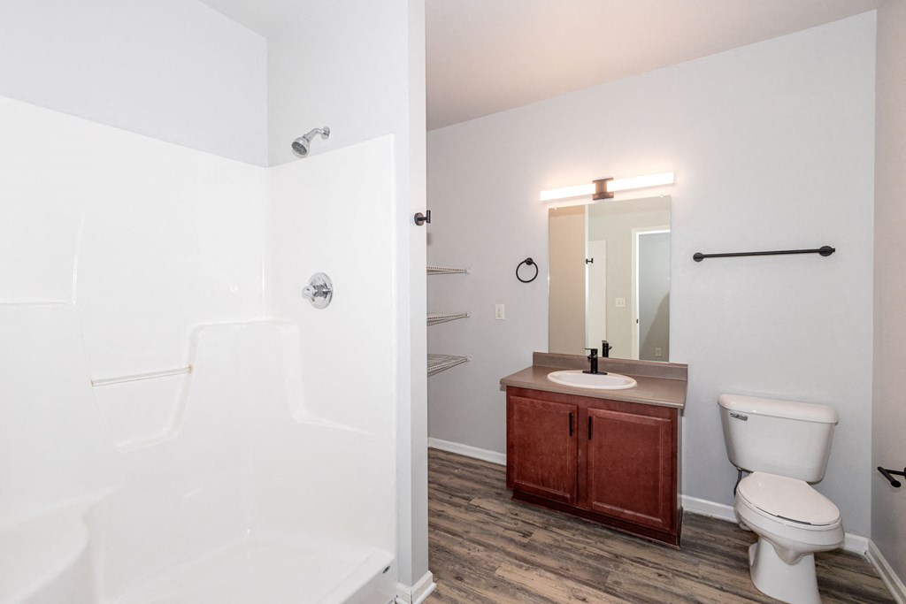 A white bathroom with a toilet, sink, and mirror at Meadowlark Place Apartments, Grimes, Iowa