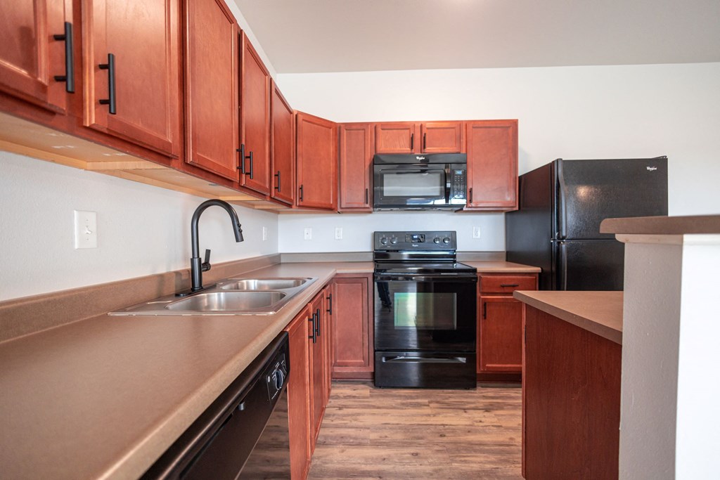 A kitchen with black appliances and wooden cabinets at Meadowlark Place Apartments, Grimes, Iowa