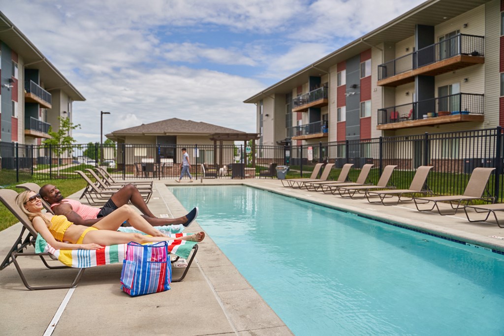 A woman in a yellow bikini lounges by a pool with a man in a pink shirt at Meadowlark Place Apartments, Grimes, IA,  50111
