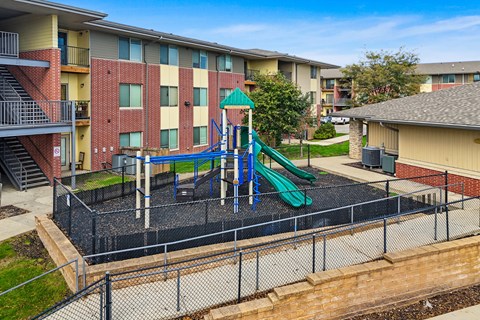 A playground with a green slide and a black fence.