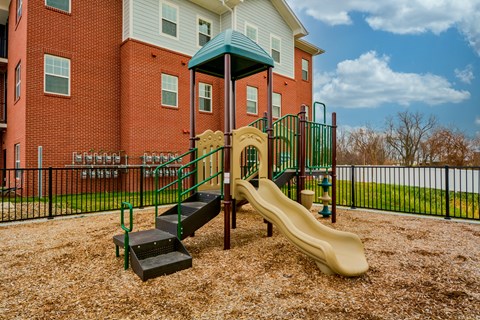 A playground with a slide and steps in front of a red brick building.