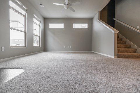 A spacious room with a carpeted floor and a staircase on the right side.