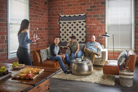 A woman is serving wine to a group of people sitting on a couch in a living room.