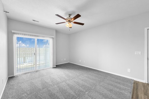 A spacious room with a ceiling fan and sliding glass doors leading to a balcony.