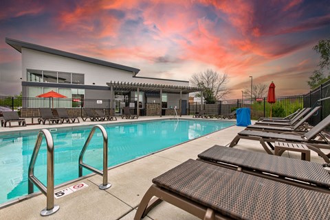 A pool with a building behind it and chairs around it.