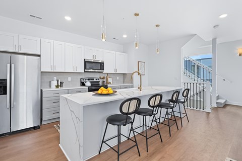 A kitchen with white cabinets and a white island with black barstools.