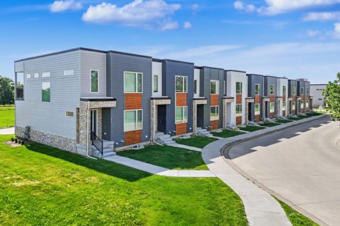 A row of modern townhouses with a sidewalk and green grass in front.
