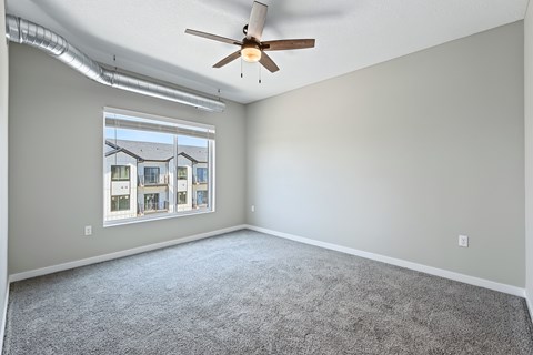 A room with a ceiling fan and a window overlooking a building.