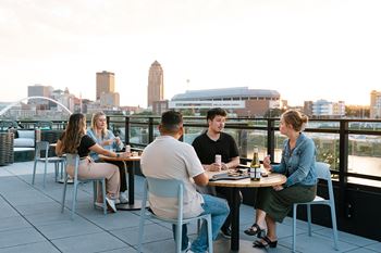 Four people are sitting at a table on a rooftop with a city skyline in the background.at Level, Iowa, 50309