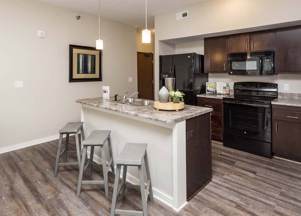 A kitchen with a granite countertop and bar stools. at Stonegate Crossing Apartments, Clive, 50325