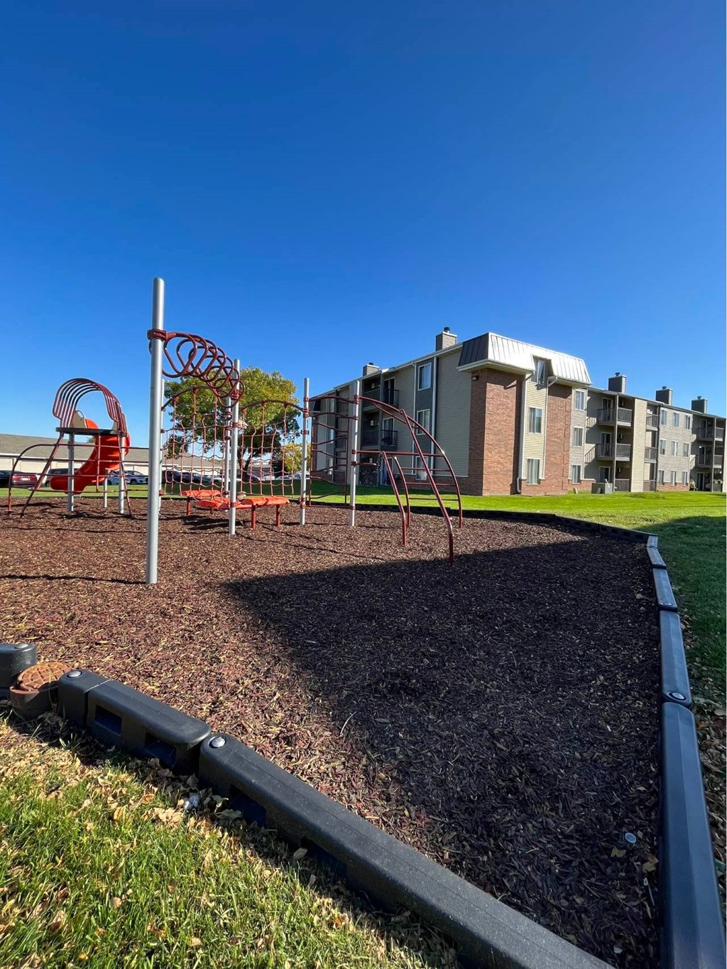 A playground with a red swing set and a play structure in the background at Penbrooke Place Apartments, Sioux Falls, South Dakota