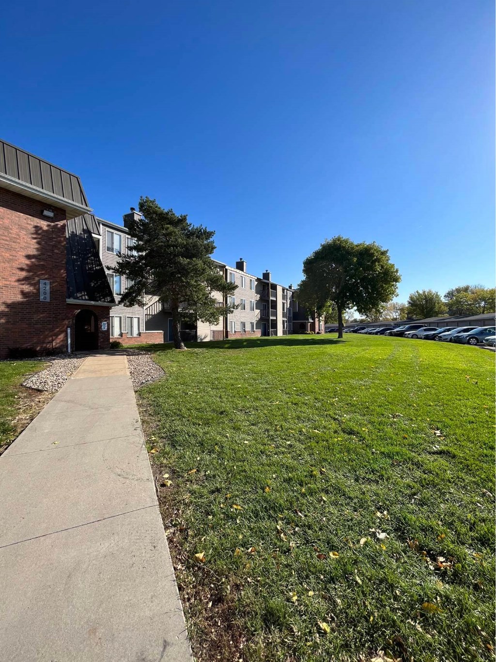 A grassy area in front of a building with a sidewalk at Penbrooke Place Apartments, South Dakota, 57106