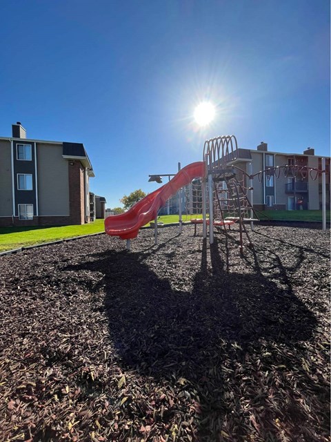A playground with a red slide and a person's shadow on the ground at Penbrooke Place Apartments, Sioux Falls, SD, 57106
