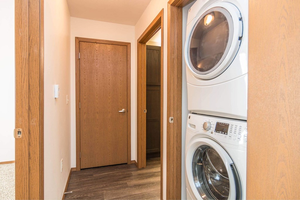 A washing machine is in a small room with a wooden door at Penbrooke Place Apartments, Sioux Falls, SD