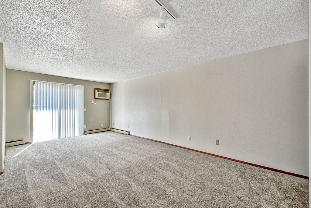 A room with a carpeted floor and a door leading to a balcony at Penbrooke Place Apartments, Sioux Falls