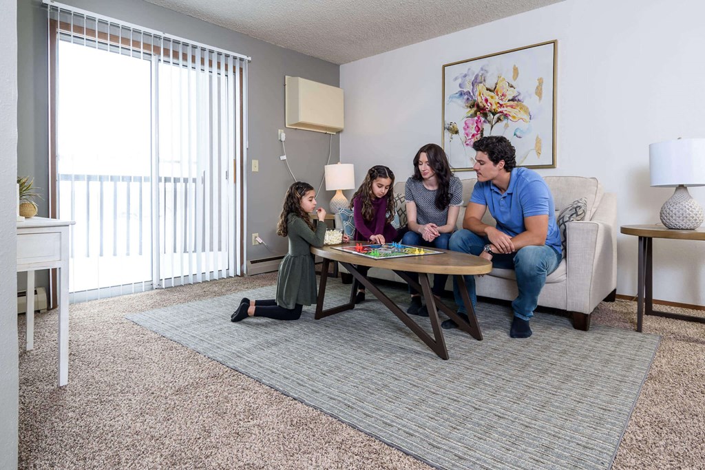 A family of four is sitting on a couch in a living room at Penbrooke Place Apartments, Sioux Falls, SD