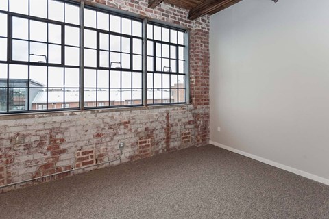 A room with a large window and a brick wall at Spaulding Lofts Apartments, Grinnell, IA, 50112