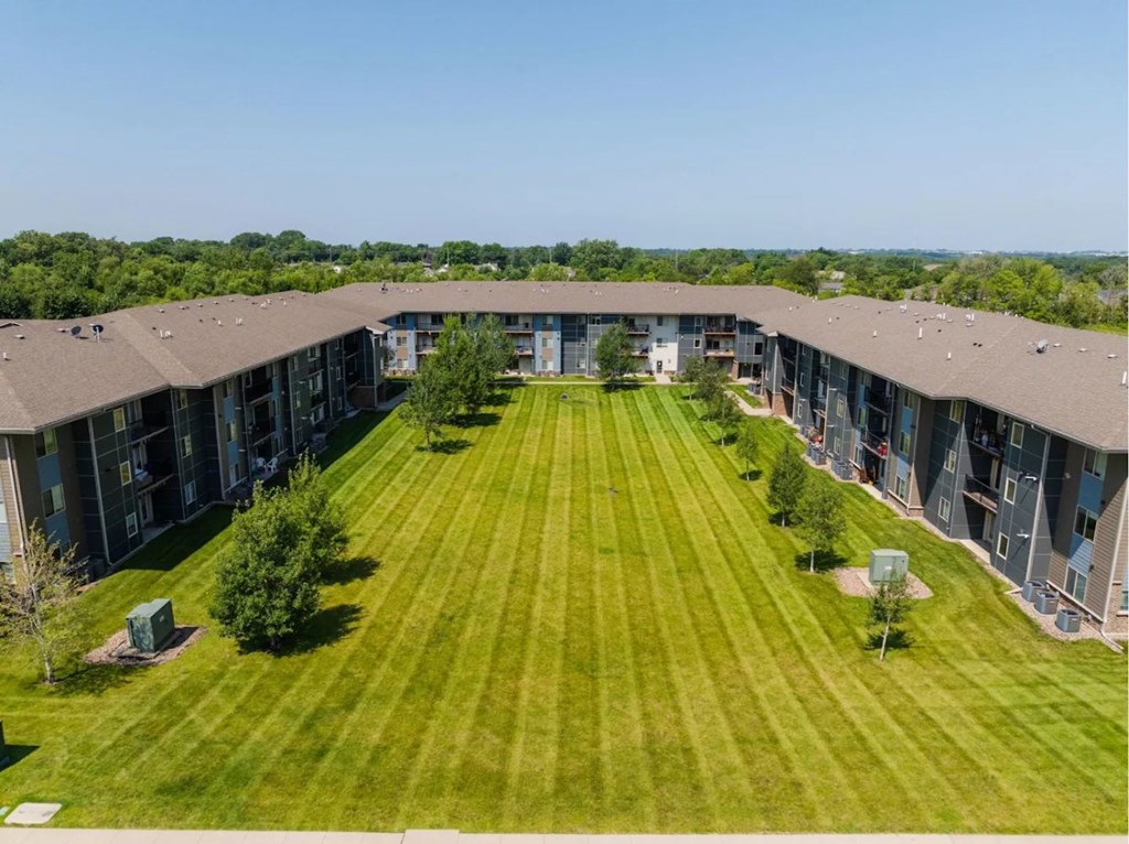 A large grassy area in front of a building with trees and bushes.