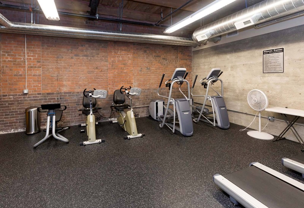 A gym with a brick wall and a variety of exercise equipment.at Riverpoint Lofts, Iowa, 50309