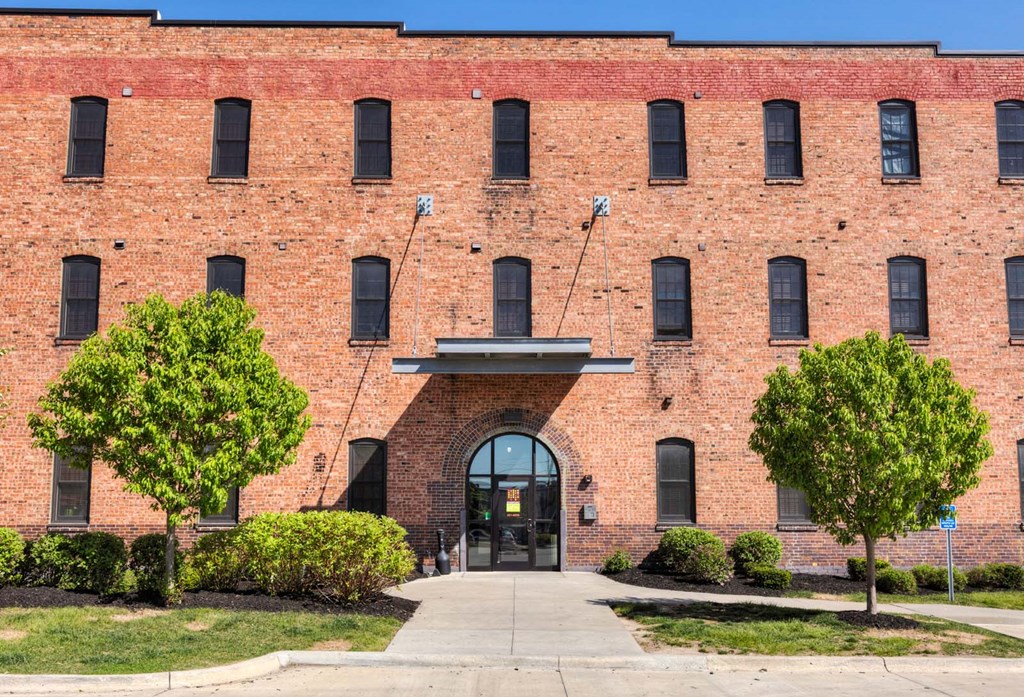 A red brick building with a large arched entrance and two trees in front.at Riverpoint Lofts, Des Moines, IA