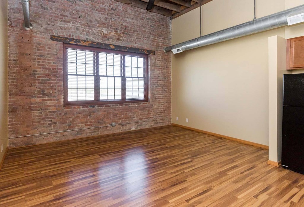 A room with wooden floors and a brick wall with a window.at Riverpoint Lofts, Des Moines, 50309