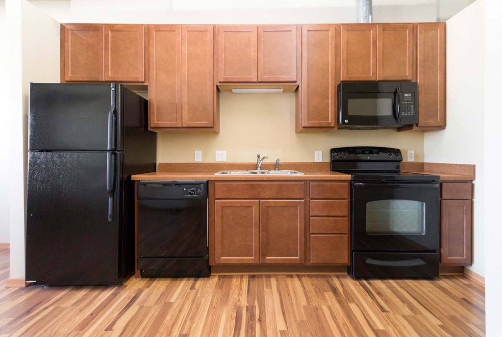 A black refrigerator, dishwasher, and oven in a kitchen with wooden cabinets.at Riverpoint Lofts, Des Moines, IA 50309