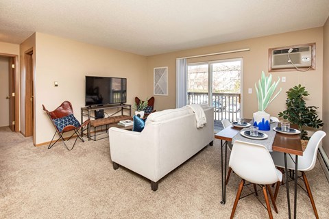 A living room with a white couch, a white chair, a white dining table and chairs, a television, and a potted plant.