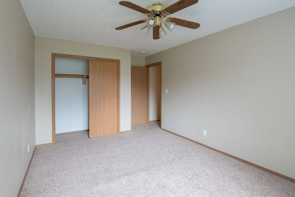 A room with a ceiling fan and carpeted floor. A room with a ceiling fan and carpeted floor at Peach Tree Apartments, Ankeny, IA, 50021