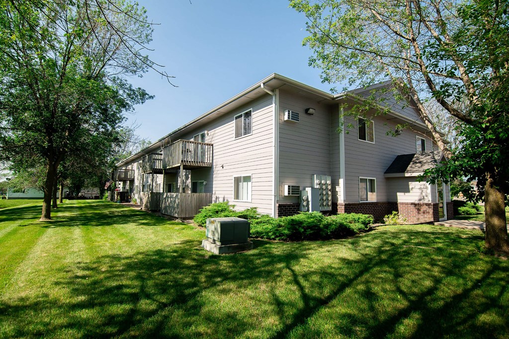 A house with a grey siding and a balcony is surrounded by green grass and trees. A house with a grey siding and a balcony is surrounded by green grass and trees at Peach Tree Apartments, Ankeny, IA